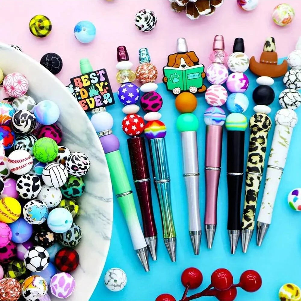 A collection of colorful 15mm printed silicone beads and various tools for DIY jewelry making arranged on a light pink backgr