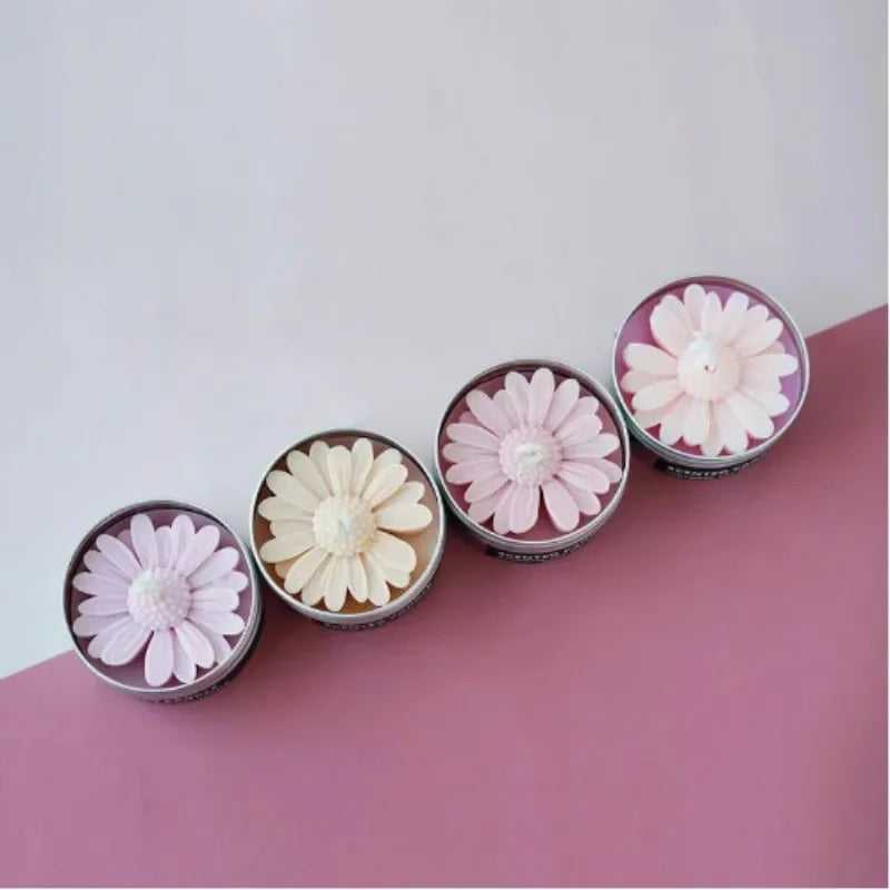 Collection de moules en silicone pour gâteaux, en forme de marguerites roses et blanches, sur une surface rose.