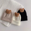 A set of three knitted baby hats featuring brown bear ears on beige, white, and black fabric.