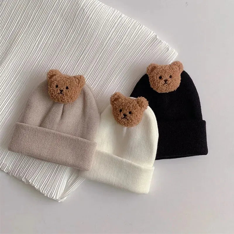 A set of three knitted baby hats featuring brown bear ears on beige, white, and black fabric.
