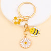 Gold enamel keychain featuring a honeycomb shape and a bee with a daisy flower design