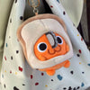 An orange Pochita plush keychain with a chainsaw detail is hanging from a gold-colored chain on a light-colored fabric bag.