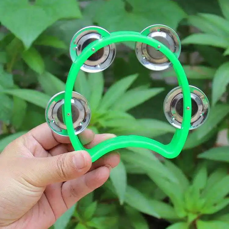 Una mano sostiene un tambor de percusión verde brillante con cascabeles plateados contra un fondo desenfocado de follaje verd