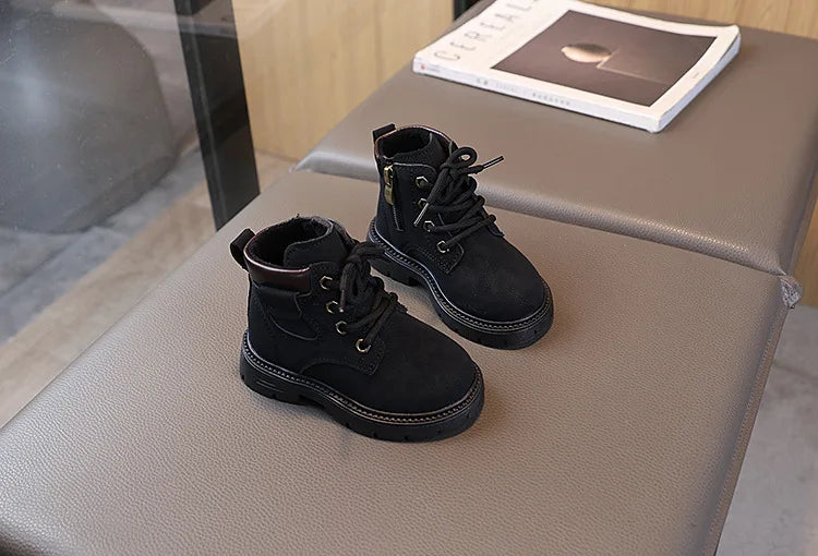 A pair of black kids' winter leather boots with laces and a side zipper resting on a gray surface.