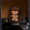 A brown wooden shelter box containing a figurine of a person with reddish hair and light skin, displayed on a dark surface.