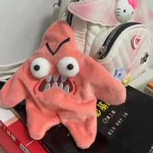 A fluffy, pink, starfish-shaped plush toy with large eyes and teeth is displayed next to a white and pink patterned bag.