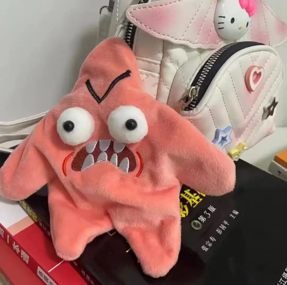 A fluffy, pink, starfish-shaped plush toy with large eyes and teeth is displayed next to a white and pink patterned bag.