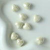 A collection of ten glossy, heart-shaped ceramic beads in an off-white or cream color arranged on a white surface.