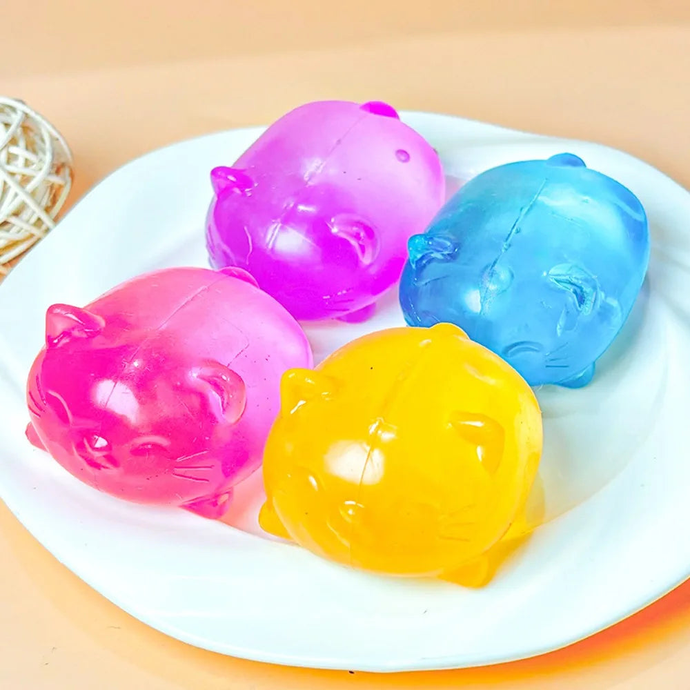 A set of three colorful plastic cat squishy stress relief toys in pink, blue, and yellow resting on a white plate.