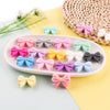 A collection of colorful silicone bow tie beads in pink, purple, blue, and green arranged on a white oval dish.