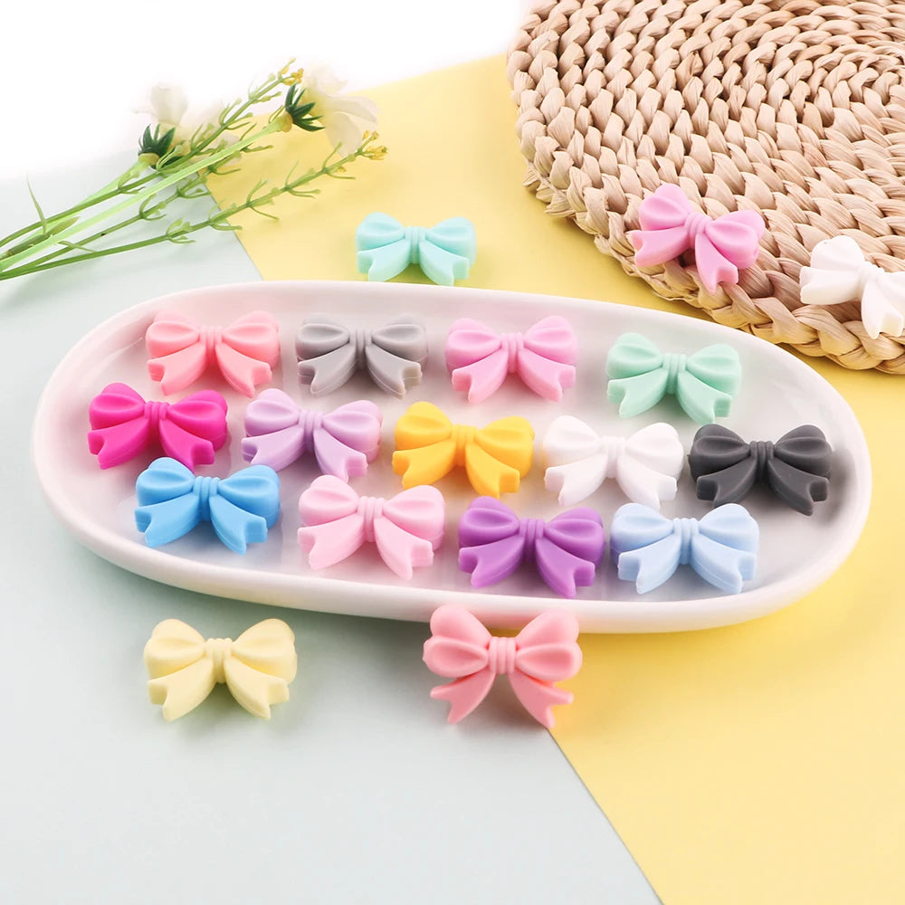 A collection of colorful silicone bow tie beads in pink, purple, blue, and green arranged on a white oval dish.