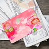 A pink card featuring cute strawberry and shortcake illustrations placed on top of US currency bills.