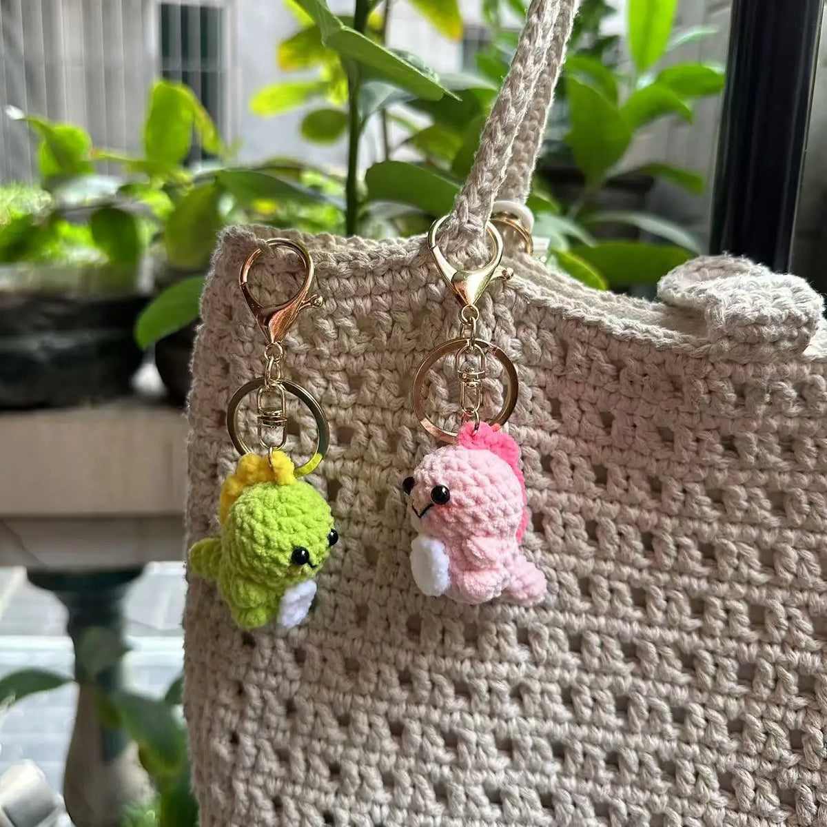 A handmade crochet dinosaur keychain with a yellow and green dinosaur charm hanging from a beige fabric bag.