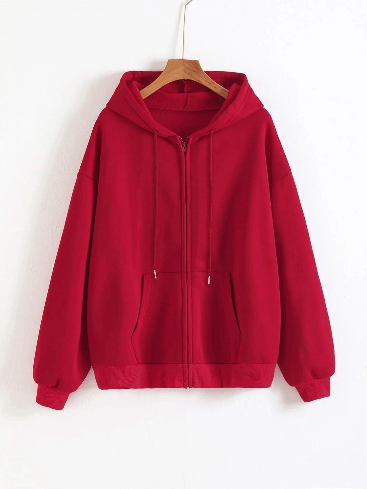 A maroon oversized zip-up hoodie hanging on a wooden hanger against a white wall.