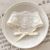 A white floral lace baby headband for newborns is displayed on a light ceramic plate.