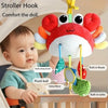 A baby is shown holding a crab-themed rattle and teether toy with a hanging strap.