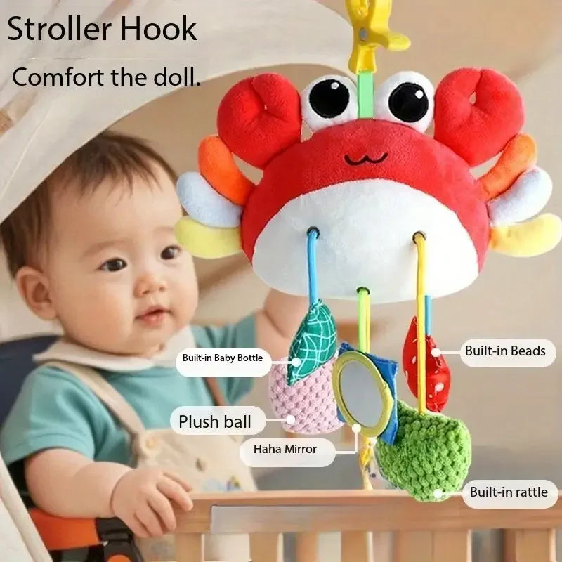 A baby is shown holding a crab-themed rattle and teether toy with a hanging strap.