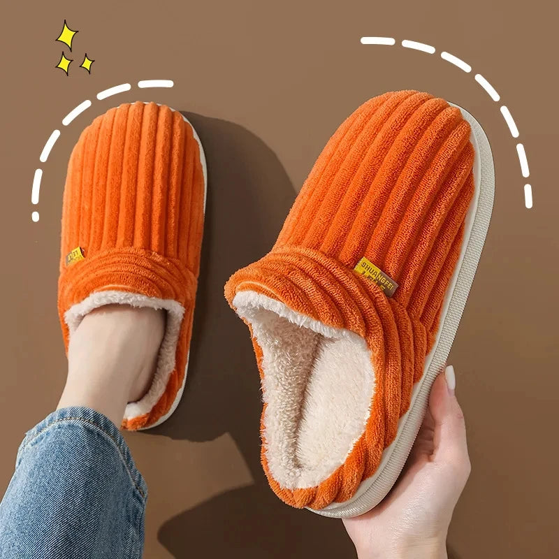 A pair of bright orange faux fur slippers being held, showing the plush interior and exterior texture.