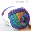 A ball of hand-dyed rainbow merino wool yarn in various shades is shown on a wooden surface.