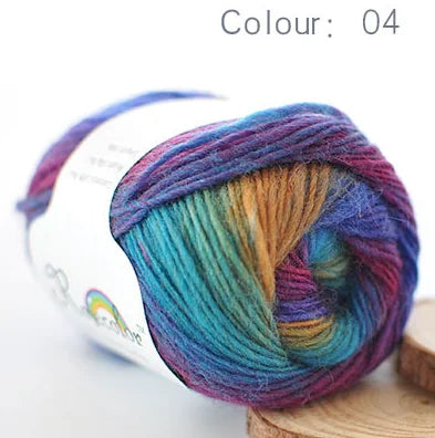A ball of hand-dyed rainbow merino wool yarn in various shades is shown on a wooden surface.