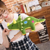 A woman smiling while holding a green dinosaur plush toy against a brick background.
