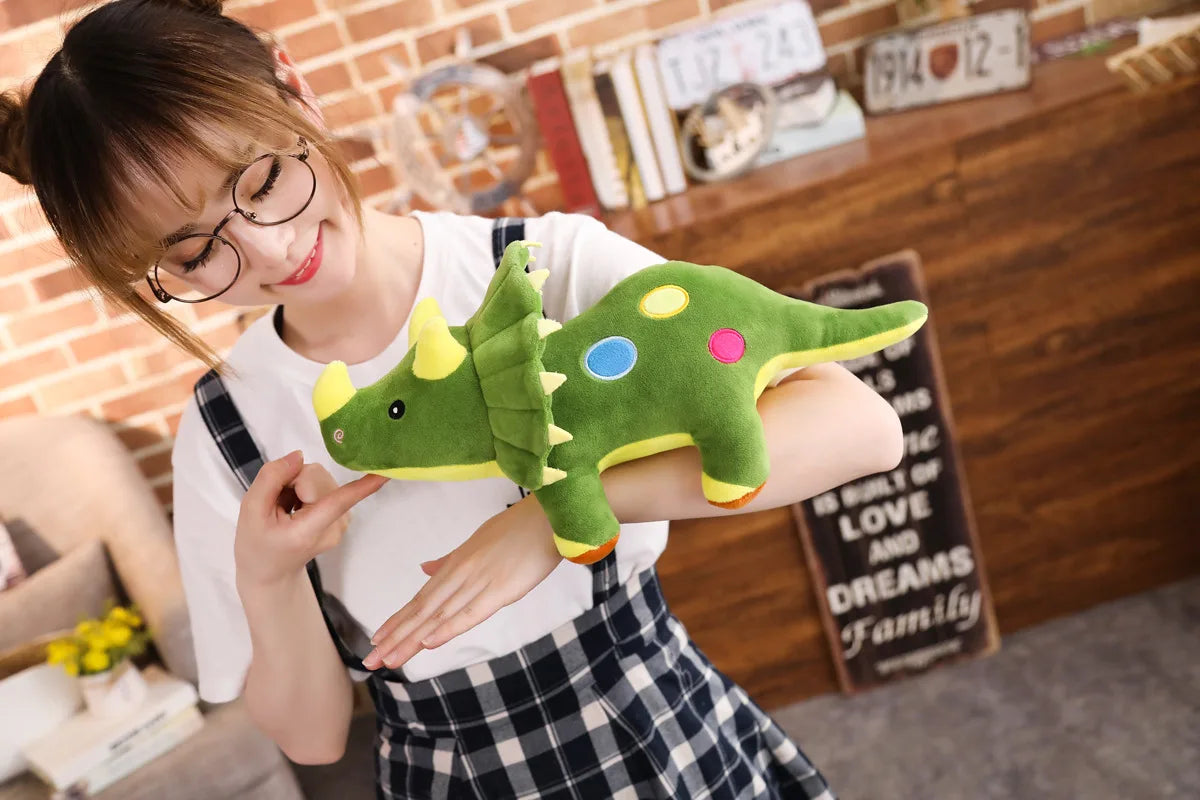 A woman smiling while holding a green dinosaur plush toy against a brick background.