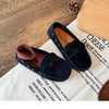 A pair of dark navy velvet slip-on moccasins with bow details resting on a white cloth.