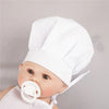 A baby wearing a white chef hat and apron for pretend play