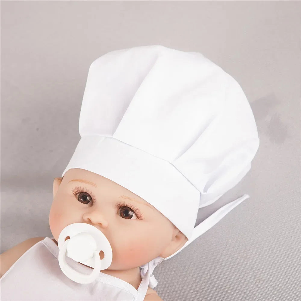 A baby wearing a white chef hat and apron for pretend play