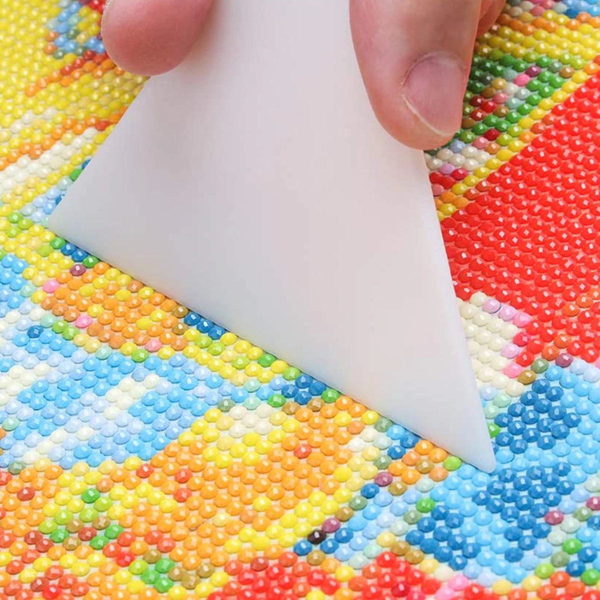 A hand holds a white diamond painting tool against a colorful fabric background.