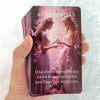 A hand holds a purple oracle card featuring two women in gowns and the text Sugerencias