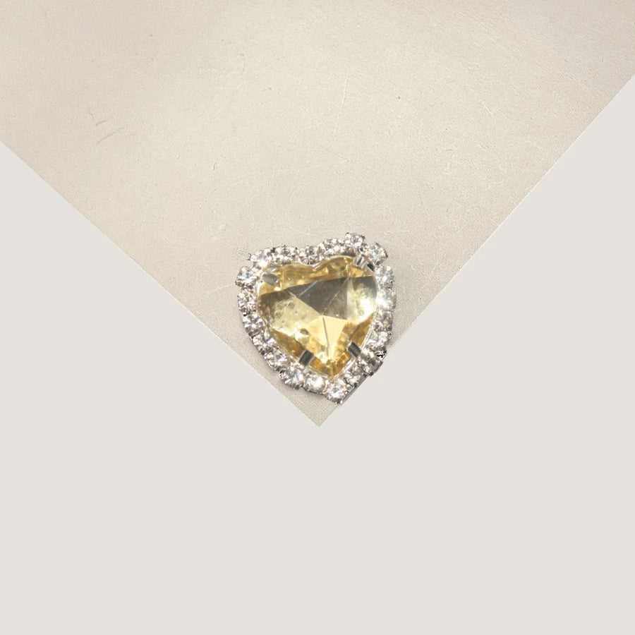 A heart-shaped flatback rhinestone embellishment for DIY crafts, set in a clear setting.