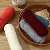 Spools of premium milk cotton yarn in various shades of red, blue, and gray resting on a woven basket.