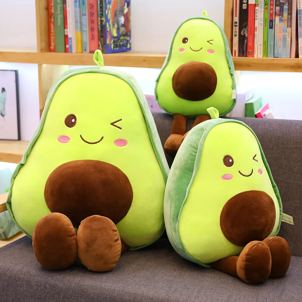 Three cute avocado plush toys in various shades of green and brown sitting on a gray surface.