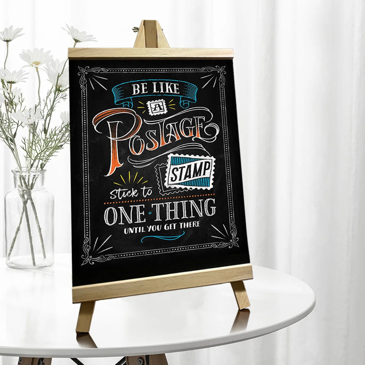 A wooden chalkboard easel displaying the phrase Be Like Postage Stick to One Thing until you get there