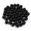 A pile of small, round, black imitation pearl beads for jewelry making.