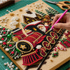 A hand is painting a Christmas scene on a diamond painting canvas using beads and sequins.