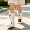 A child wearing white waterproof bear rain boots with anti-slip soles walking on a paved path.