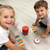 Two children are playing a colorful speed bead grabbing board game on a light wooden floor.