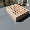 A wooden box filled with colorful acrylic gemstones arranged in a grid on a glass table.