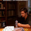 A man is working on a detailed astronomical clock 3D metal puzzle kit on a wooden table surrounded by bookshelves.
