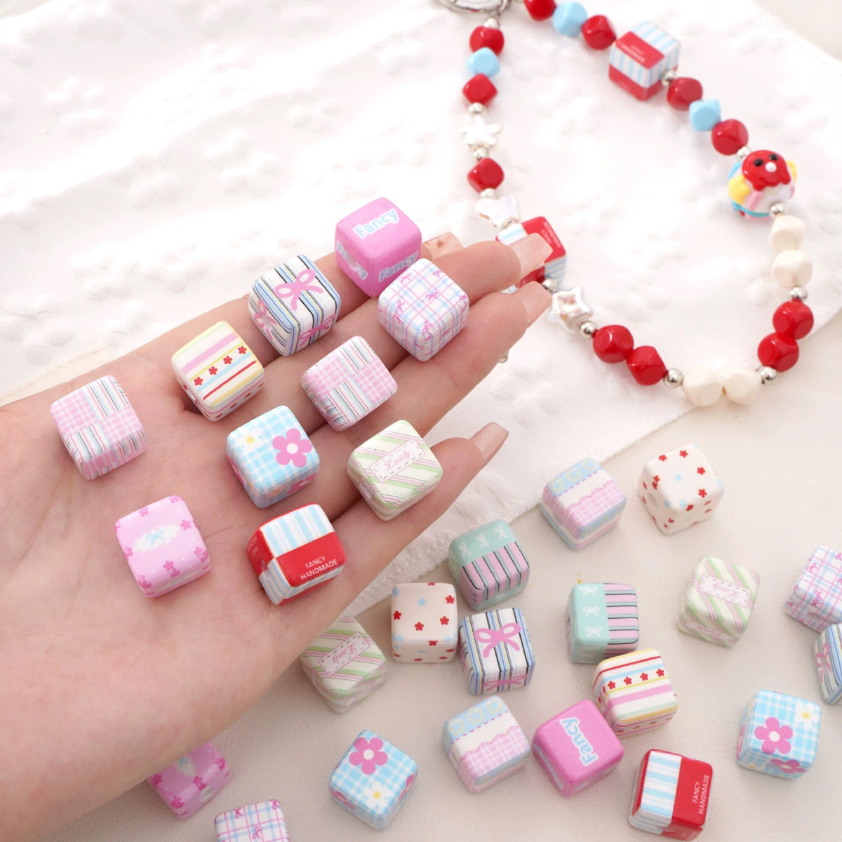 A hand displays pink acrylic flower print beads with bow charms for DIY accessories, strung on a white beaded necklace.