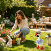 A woman sits in a garden surrounded by flowers and decorative geese figurines.