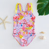 A pink and purple mermaid unicorn one-piece swimsuit with yellow trim is displayed on a white surface next to starfish.