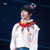 A person wearing a white shirt with a red and yellow ruffled collar, performing on stage.