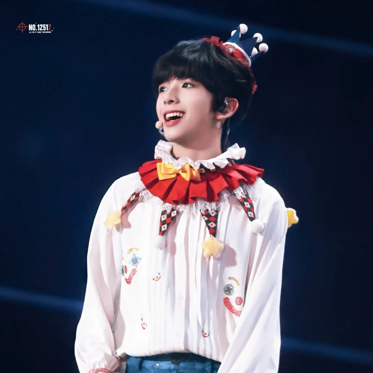 A person wearing a white shirt with a red and yellow ruffled collar, performing on stage.