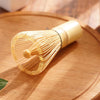 A traditional bamboo matcha whisk set with fine wires resting on a wooden plate.