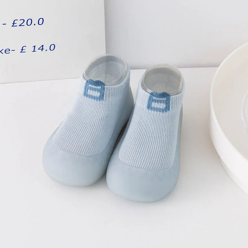 A pair of light blue knitted soft sole sock shoes for babies and toddlers with blue accents.