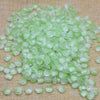 A pile of translucent light green tulip flower glass beads scattered on a beige fabric surface.