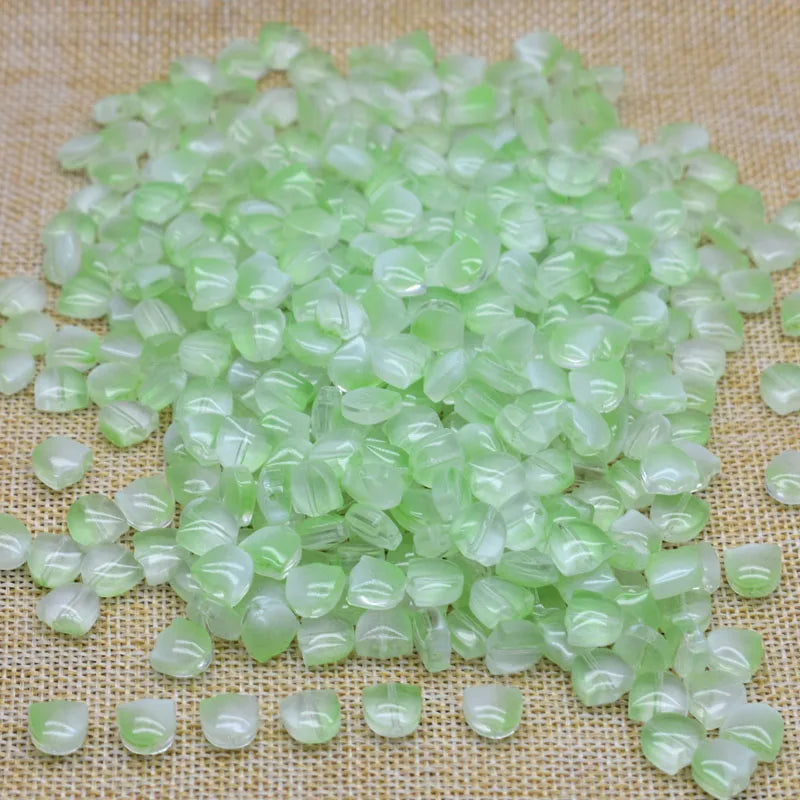 A pile of translucent light green tulip flower glass beads scattered on a beige fabric surface.
